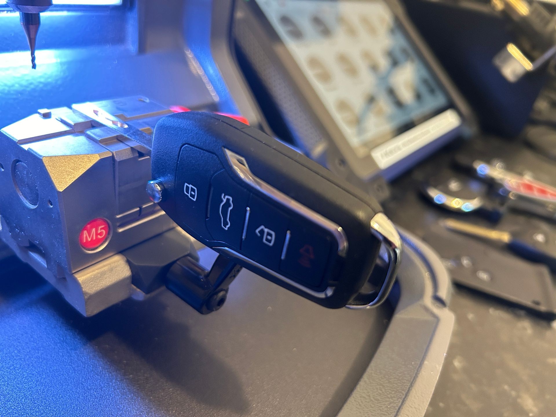 Close-up of a car key being duplicated using an automated cutting machine in a workshop.