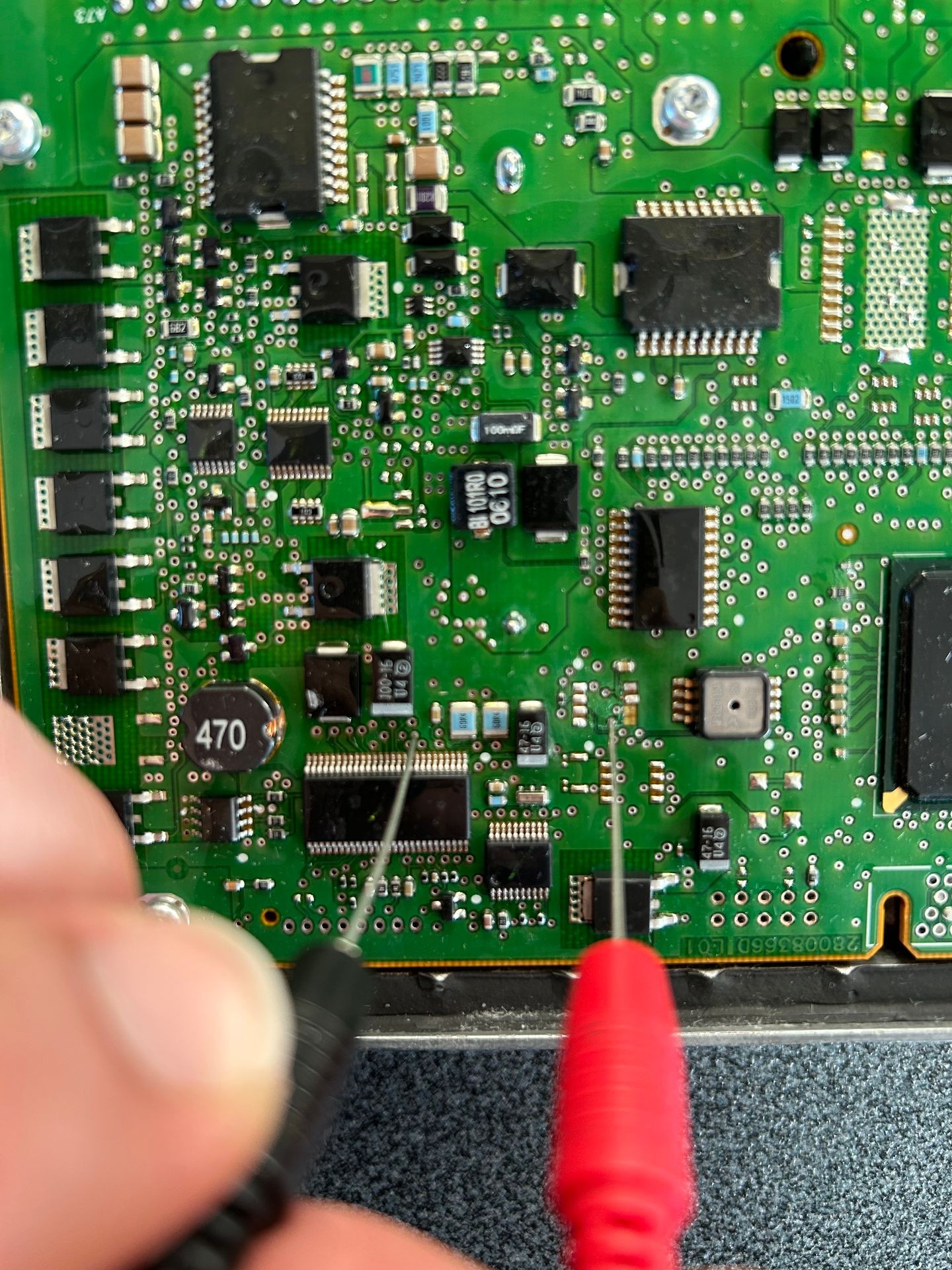 Close-up of a green circuit board with various electronic components and two probes testing the connections.