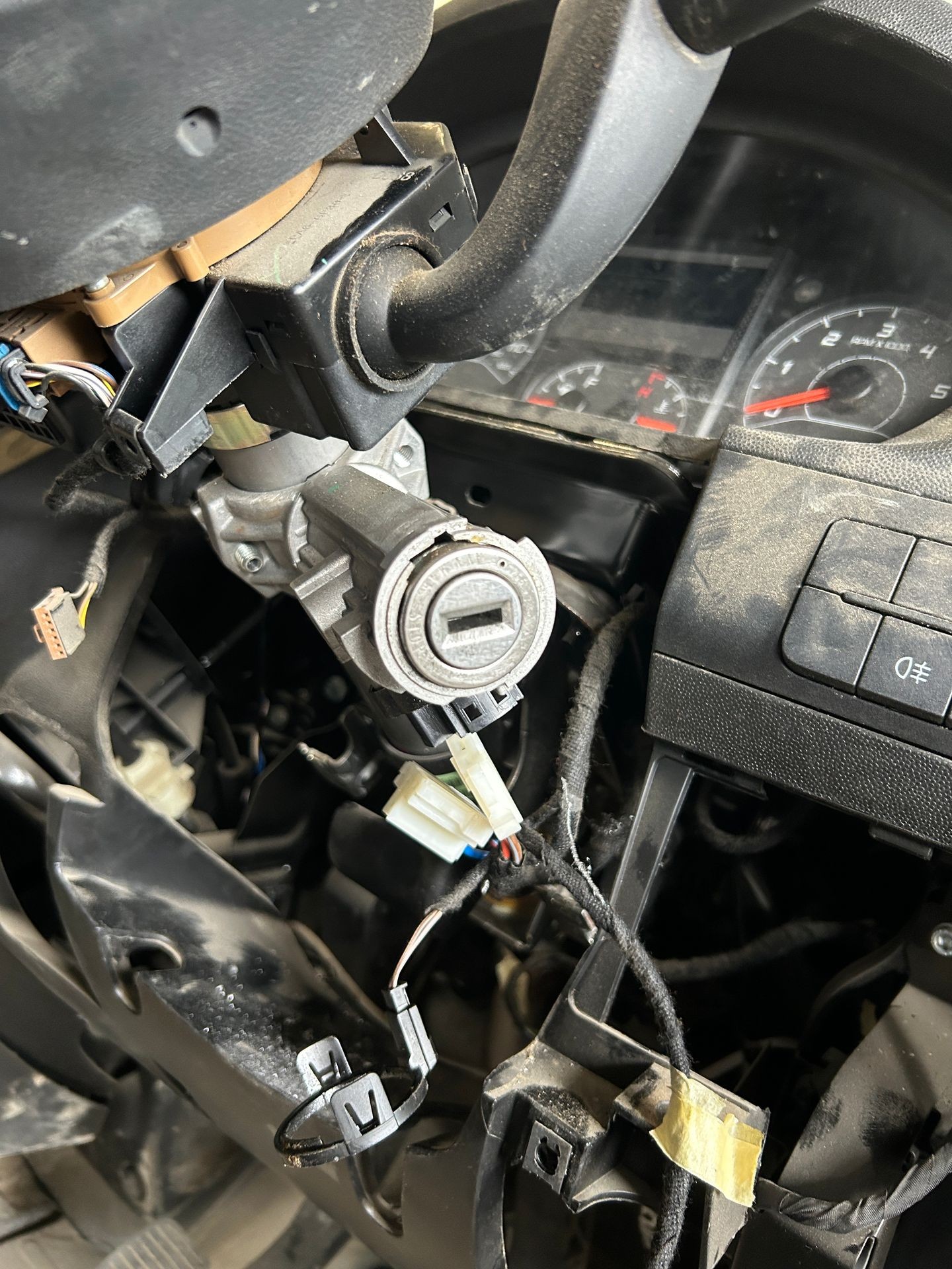 Close-up of a disassembled car steering column with exposed wires and ignition switch components.